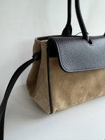A close-up of 2026 Chanel East West structured handbag in beige quilted suede with black pebbled leather trim, handles, and side knotted accent
