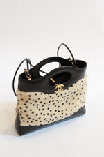 Close-up of side angle of Chanel mini shopping tote with ivory calf hair hand-painted cheetah dot print, black leather trim, structured top handle from Métiers d'Art 2026 collection by Matthieu Blazy 