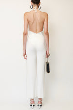 Back view of Chanel white halterneck swimsuit with ruffled scalloped edges throughout, CC logo detail, and high cut leg. Paired with vintage Plein Sud sheer mesh white pants, Chanel Ritz Coco Minaudière Leather Clutch, Chanel T-Strap piano sandals, Alaia leather hoop earrings.