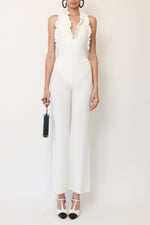 Front view of Chanel white halterneck swimsuit with ruffled scalloped edges throughout, CC logo detail, and high cut leg. Paired with vintage Plein Sud sheer mesh white pants, Chanel Ritz Coco Minaudière Leather Clutch, Chanel T-Strap piano sandals, Alaia leather hoop earrings.