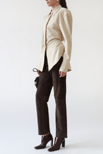 Angled view of vintage Gucci dark brown leather V-cut booties with a square toe and angular heel, styled with The Frankie Shop beige structured shirt, vintage Gucci brown suede trousers, and Miu Miu brown nappa leather shoulder bag.