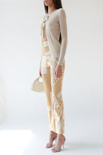 Side view of Hermès ivory and camel silk bridle print pants with a high waist and silver horsebit hardware, styled with an Armani ivory ribbed bow-tie cardigan and Miu Miu silver heels, Christian Dior patent leather bondage bag.