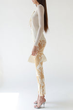 Side view of Hermès ivory and camel silk bridle print pants with a high waist and silver horsebit hardware, styled with an Armani ivory ribbed bow-tie cardigan and Miu Miu silver heels, Christian Dior patent leather bondage bag.