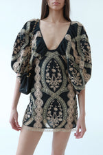 Close-up of vintage Sheri Bodell mini dress with forest and champagne lace-appliqué embroidery, plunging V-neckline, balloon sleeves, scalloped lace hem paired with vintage black classic flap Chanel bag 