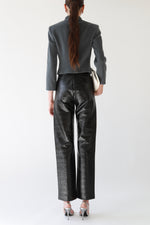 Back view of black waxed TOTEME trousers with high waist and front seam detailing, styled with Emporio Armani cropped gray wool tailored jacket, Galliano Dior bondage patent leather white top handle bag, and silver Miu Miu slingback heels  