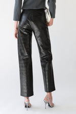 Close-up of black waxed TOTEME trousers with high waist and front seam detailing, styled with Emporio Armani cropped gray wool tailored jacket, Galliano Dior bondage patent leather white top handle bag, and silver Miu Miu slingback heels  