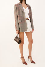 Side view of a white pleated Gucci tennis skirt with a striped waistband, styled with a vintage Escada patchwork houndstooth blazer,  Yves Saint laurent white sweetheart vest, and Manolo Blahnik red ankle-strap heels.